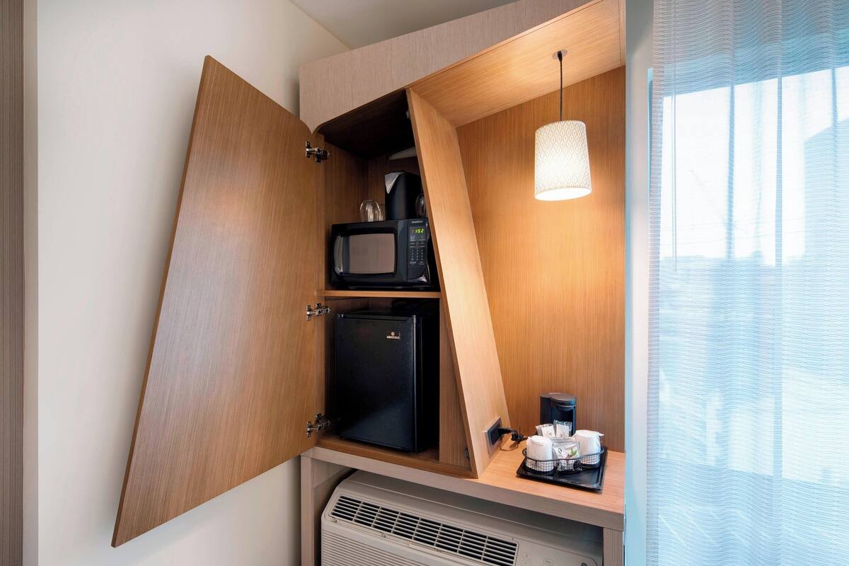 Eine kompakte Küchenzeile mit Mikrowelle, Minikühlschrank und Kaffeemaschine, mit Holzschränken und einer Pendelleuchte.