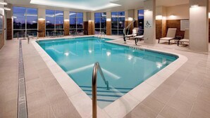 Ein Hallenbad mit Lifter, Sitzgelegenheit und großen Fenstern mit Blick auf den Abendhimmel.