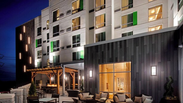 Ein modernes Hotel mit Außenbestuhlung, großen Fenstern und einem gut beleuchteten Eingangsbereich.