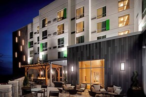 Fachada moderna de hotel con asientos exteriores, ventanas amplias y una entrada bien iluminada.