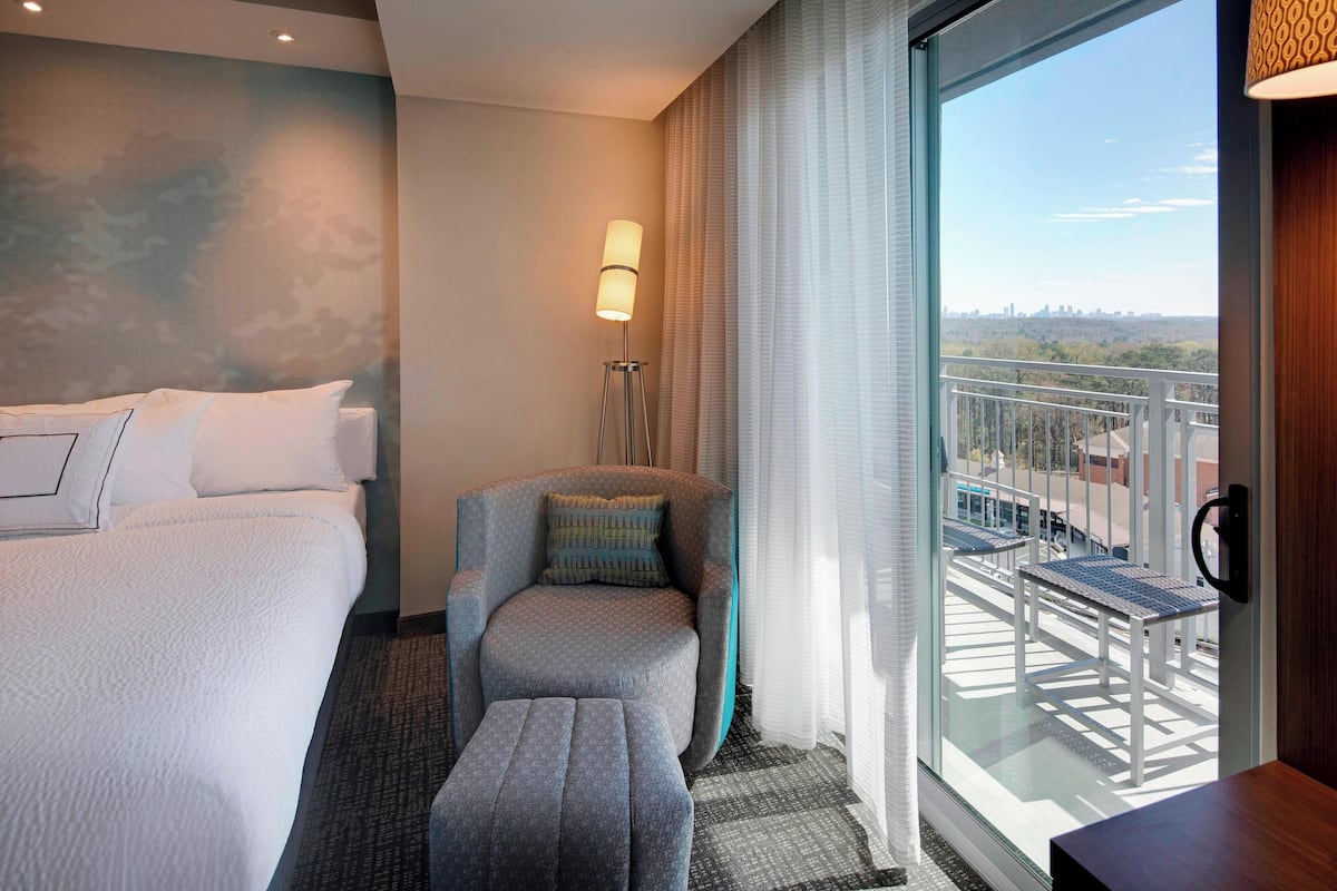 Ein Hotelzimmer mit Bett, Sessel, kleinem Tisch, Stehlampe und Balkon mit Sitzgelegenheit.