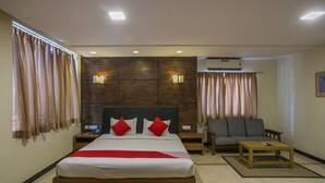 A bedroom with a bed, nightstands, a sofa, a coffee table, and an air conditioning unit.