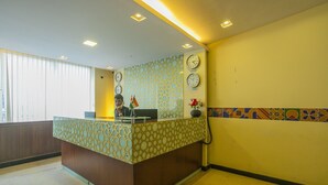 A reception desk with a patterned design, clocks on the wall, and a window with blinds.