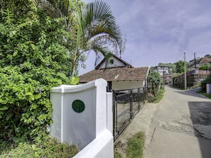 A residential area with a white house, a paved road, and lush greenery.