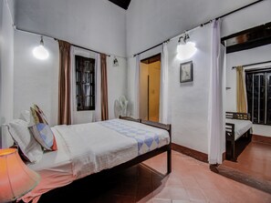 A room with a bed, a bedside table, a lamp, a window with curtains, a door, and a wall-mounted light fixture.