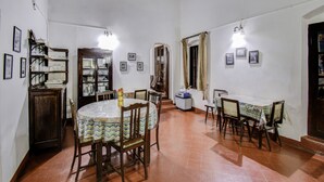 Un coin repas comprenant une table ronde, des chaises, un buffet contenant de la verrerie et une fenêtre avec des rideaux.