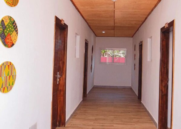 Een hal met houten vloeren en deuren, een raam met roze jaloezieën, en decoratieve wandkunst.