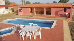 A swimming pool with a table and chairs, a building with a red roof, and a grassy area.