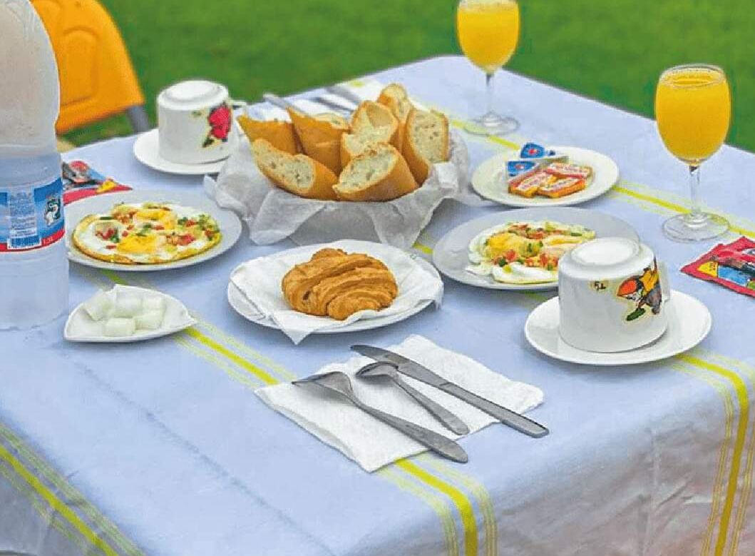 A table set with breakfast items including croissants, pastries, and a fruit plate, with drinks and cups.