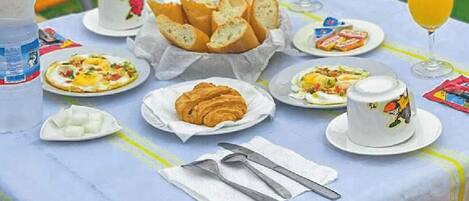 A table set with breakfast items including croissants, pastries, and a fruit plate, with drinks and cups.