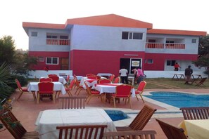 A building with a red and white facade, outdoor dining area with red chairs and white tables, and a swimming pool.