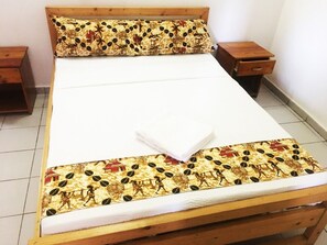 A bed with a patterned bedspread and matching pillow, wooden headboard, two bedside tables, and a tiled floor.