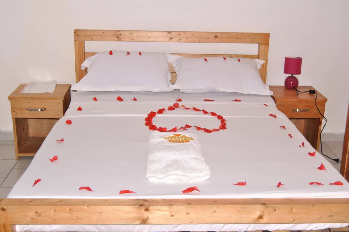 A neatly made bed with white linens, a wooden headboard, and a red flower garland.