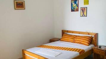 Ein Zimmer mit einem Einzelbett, einem hölzernen Kopfteil, einem Nachttisch, einem Deckenventilator und einer Wand-Klimaanlage.