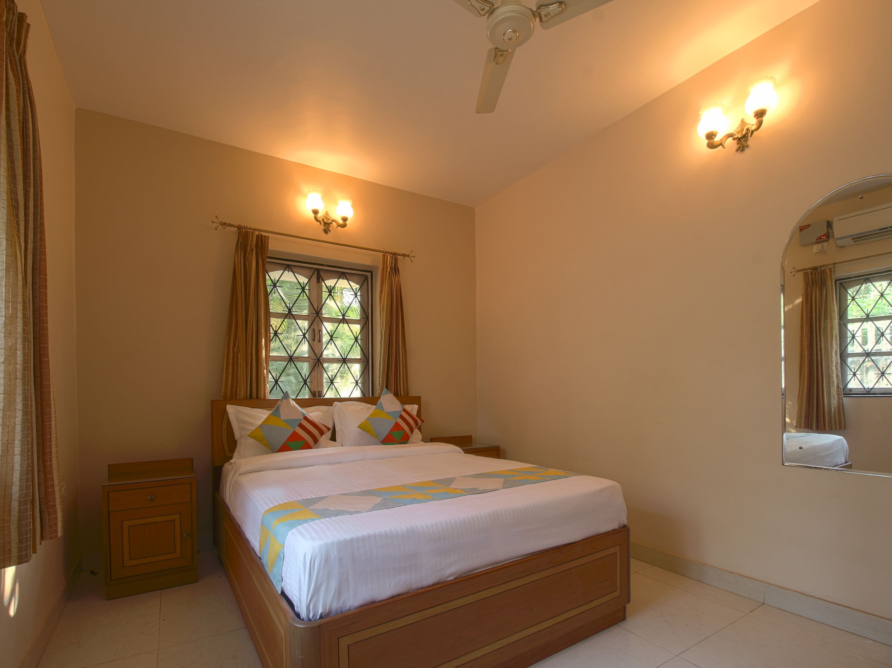 A bedroom with a bed, nightstands, a ceiling fan, a window with curtains, and wall-mounted lighting.