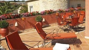 Una terraza en la azotea con paredes de piedra, una torre de piedra y mobiliario exterior con cojines naranja.