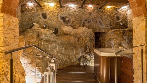 Un túnel de paredes de piedra con una escalera de madera que lleva a un área de hidromasaje.