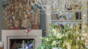 Un candelabro con múltiples brazos y luces similares a velas, una chimenea con un cuadro encima, y una mesa con un arreglo floral y libros.