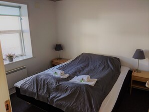 Une chambre d’hôtel avec un lit simple, deux tables de chevet, une fenêtre donnant sur un paysage agréable et une plante en pot.