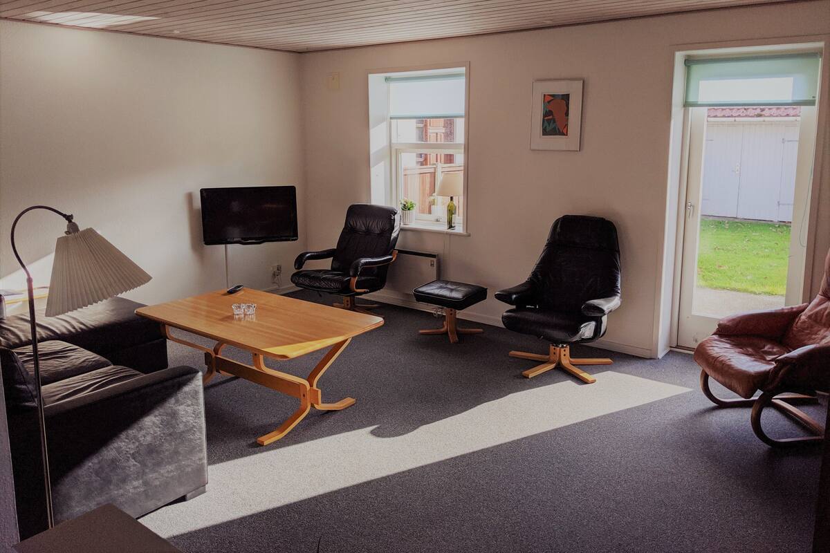 A room with a wooden table, two black leather chairs, a brown leather chair, a TV, and a window with a view of a building.