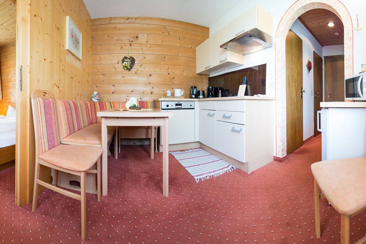 A cozy room with a bed, a wooden bench, a small table, and a kitchenette.
