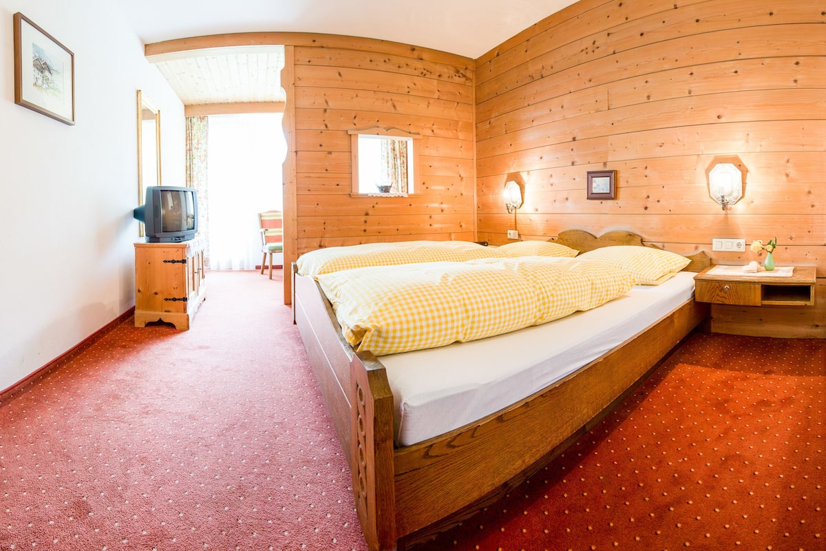 A wooden room with a bed, a television on a cabinet, and a chair.