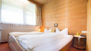 A double bed with white linens in a wooden room with a window and a bedside table with a lamp. - Pension Grubenhof (Fulpmes)
