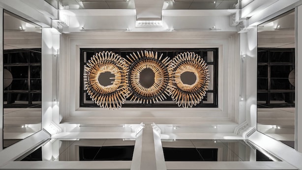 Un intérieur moderne avec une œuvre d’art centrale, des murs blancs et un sol réfléchissant.
