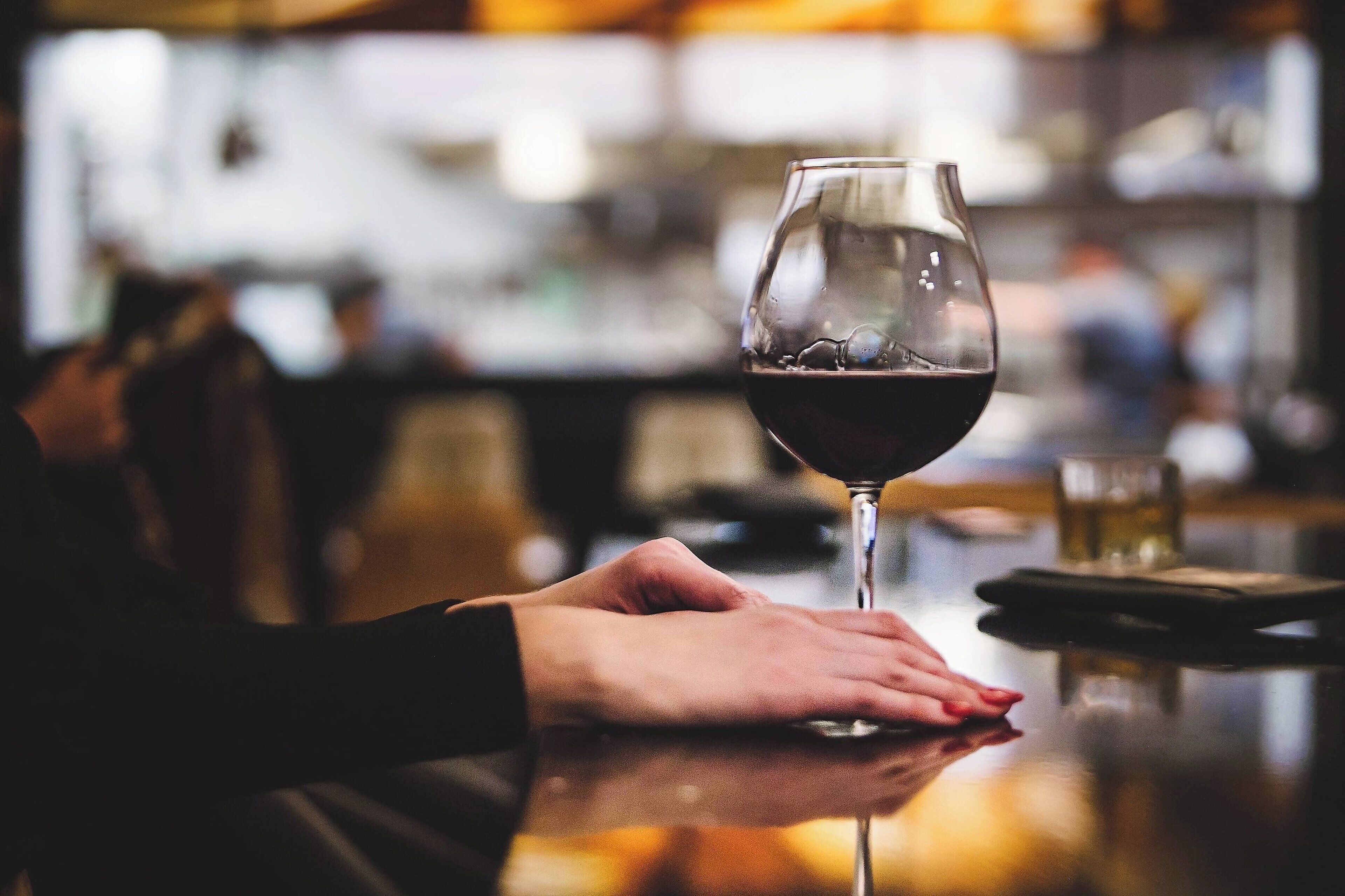 Una persona sosteniendo una copa de vino en un bar, con el fondo desenfocado.