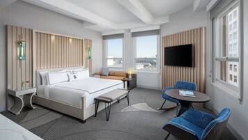Een moderne hotelkamer met een groot bed, een bureau, twee stoelen, een televisie en grote ramen.