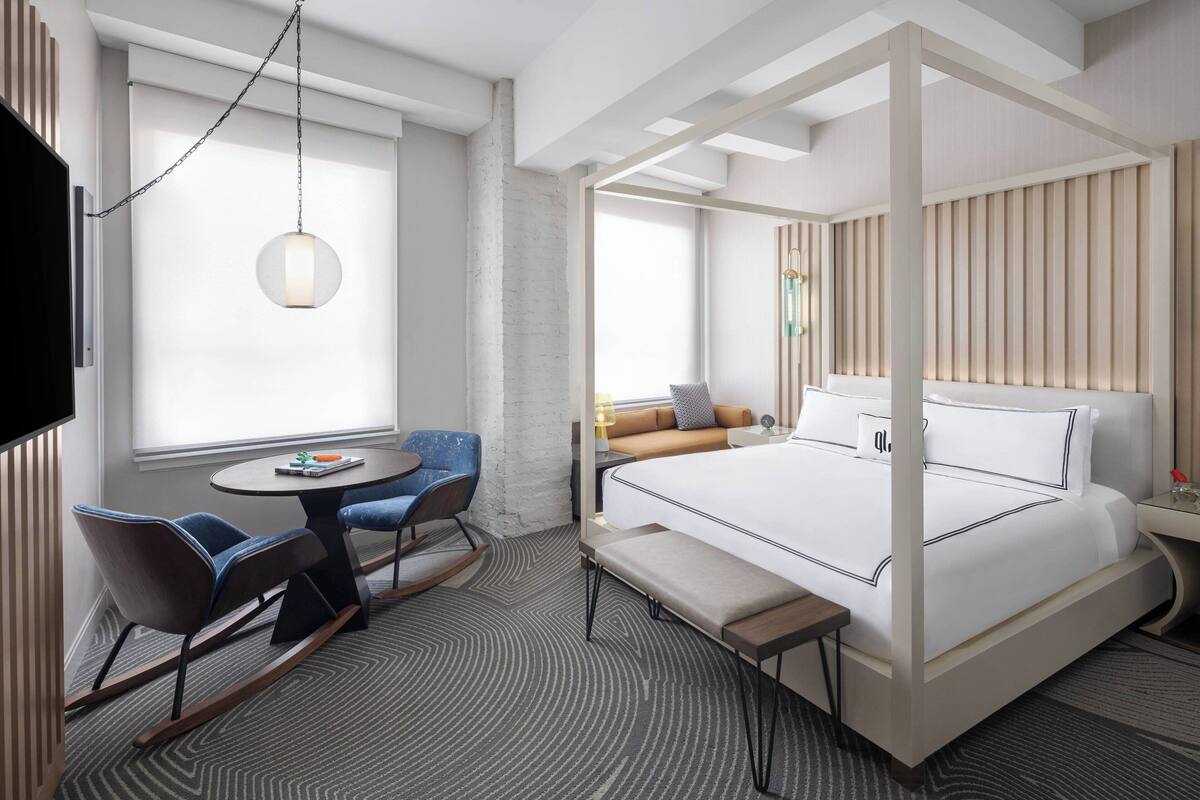 Una camera d'albergo moderna con un letto a baldacchino, una piccola zona pranzo con un tavolo rotondo e sedie, e un'ampia finestra che offre luce naturale.