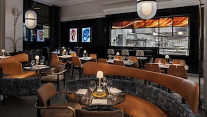 Un restaurant moderne avec des tables rondes, des sièges en cuir et une vue sur la cuisine.