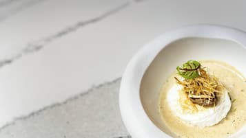Un tazón blanco con una crema para sopa y una porción de alimento blanco, posiblemente un postre, sobre una superficie de mármol.