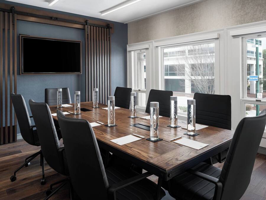 Een vergaderruimte met een lange tafel, zwarte stoelen en een groot scherm.
