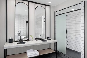 A modern bathroom with two sinks, a large mirror, and a glass shower enclosure. - Glass Light Hotel & Gallery, Autograph Collection (Norfolk)