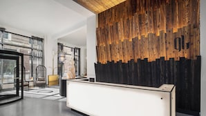 Un espace d’accueil moderne agrémenté d’un mur d’accent en bois, d’un comptoir de réception et d’un coin salon avec une chaise et une petite table.