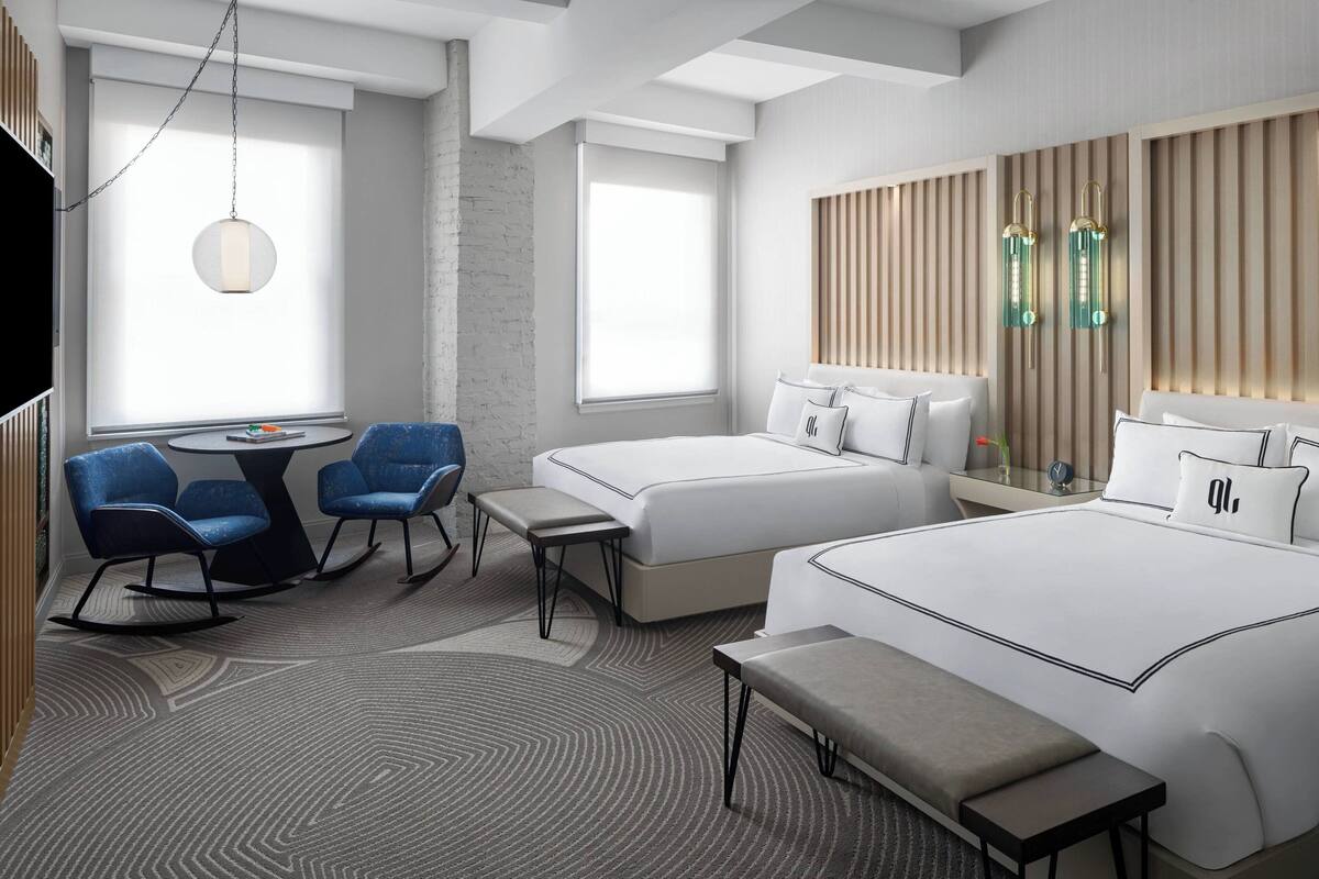 Una camera d'albergo moderna con un letto grande, due letti più piccoli, una scrivania con sedie e una zona salotto con una panca.