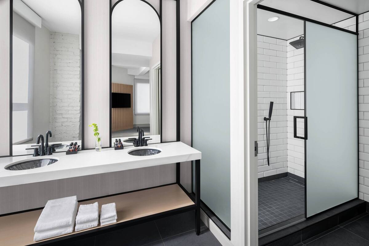 Un bagno moderno con due lavandini, uno specchio e una cabina doccia in vetro.