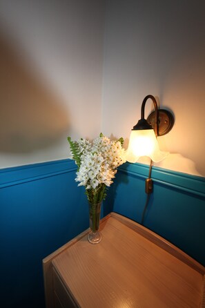 Um canto com mesa de madeira, um vaso de flores brancas e um candeeiro fixado na parede.