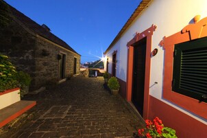 Una estrecha calle adoquinada flanqueada por edificios con fachadas de piedra y pintadas, que conduce a una vista distante de un puente.