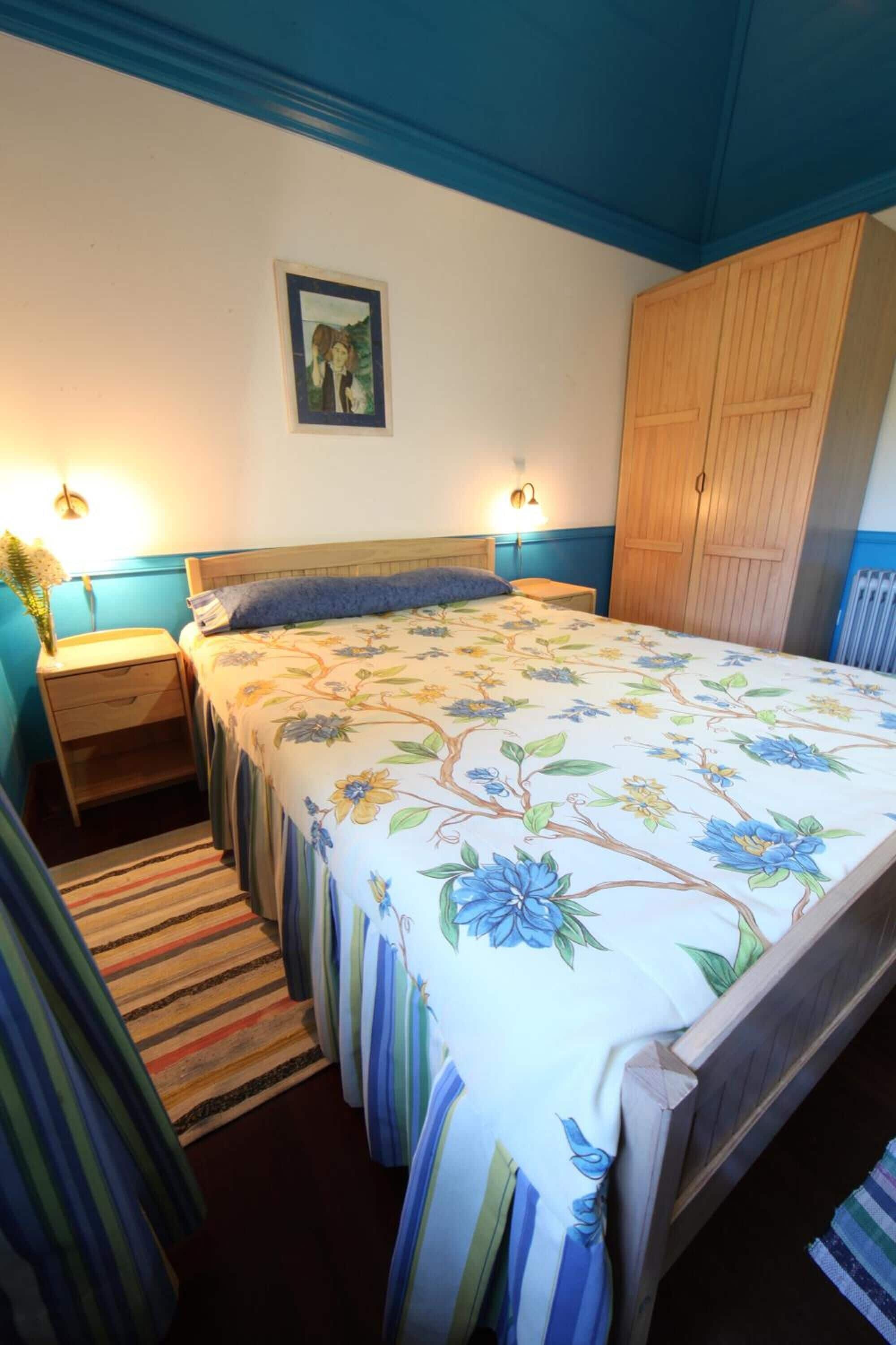 A bedroom with a floral bedspread, wooden wardrobe, and two bedside lamps.