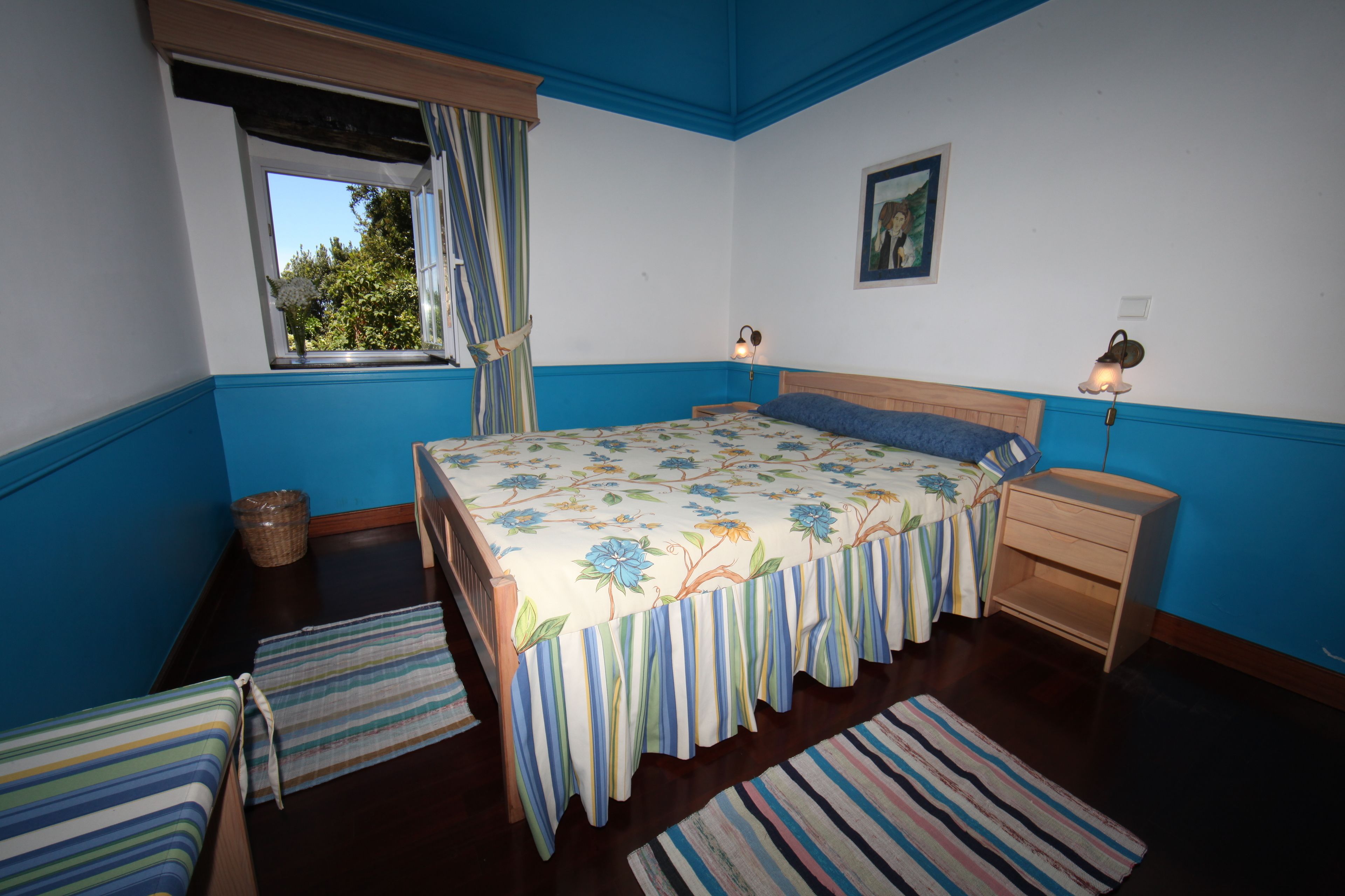 Une chambre à coucher avec un lit, des tables de chevet, une fenêtre avec des rideaux, une commode et un tableau au mur.