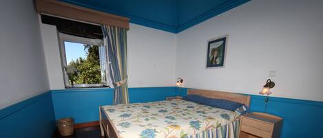 A bedroom with a bed, bedside tables, a window with curtains, a nightstand, and a painting on the wall.