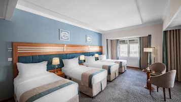 Una habitación de hotel con tres camas, una zona de estar con una silla, una mesa y una lámpara.
