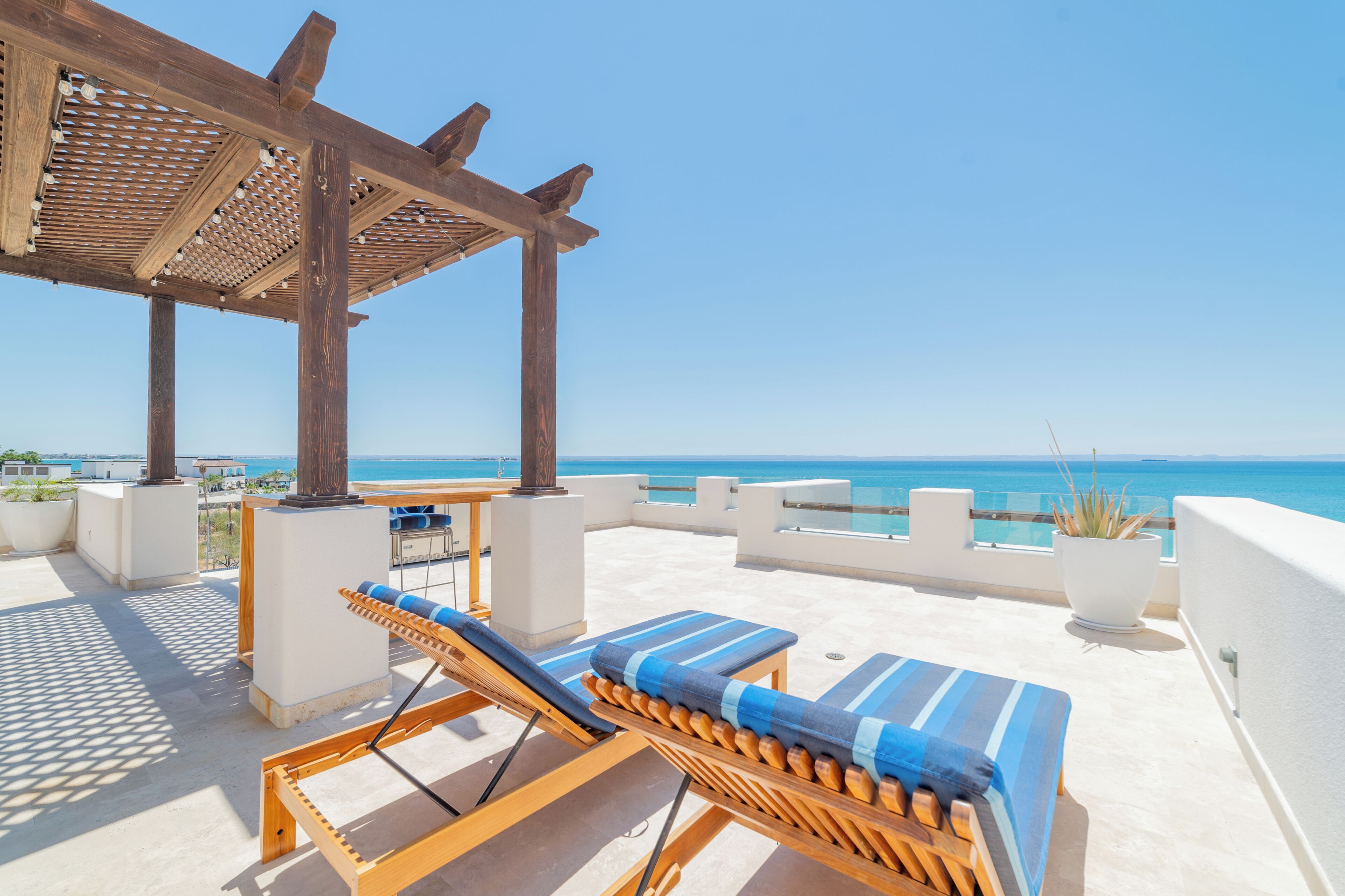 Una terraza en la azotea con sillones de madera, un pérgola y vistas al mar.
