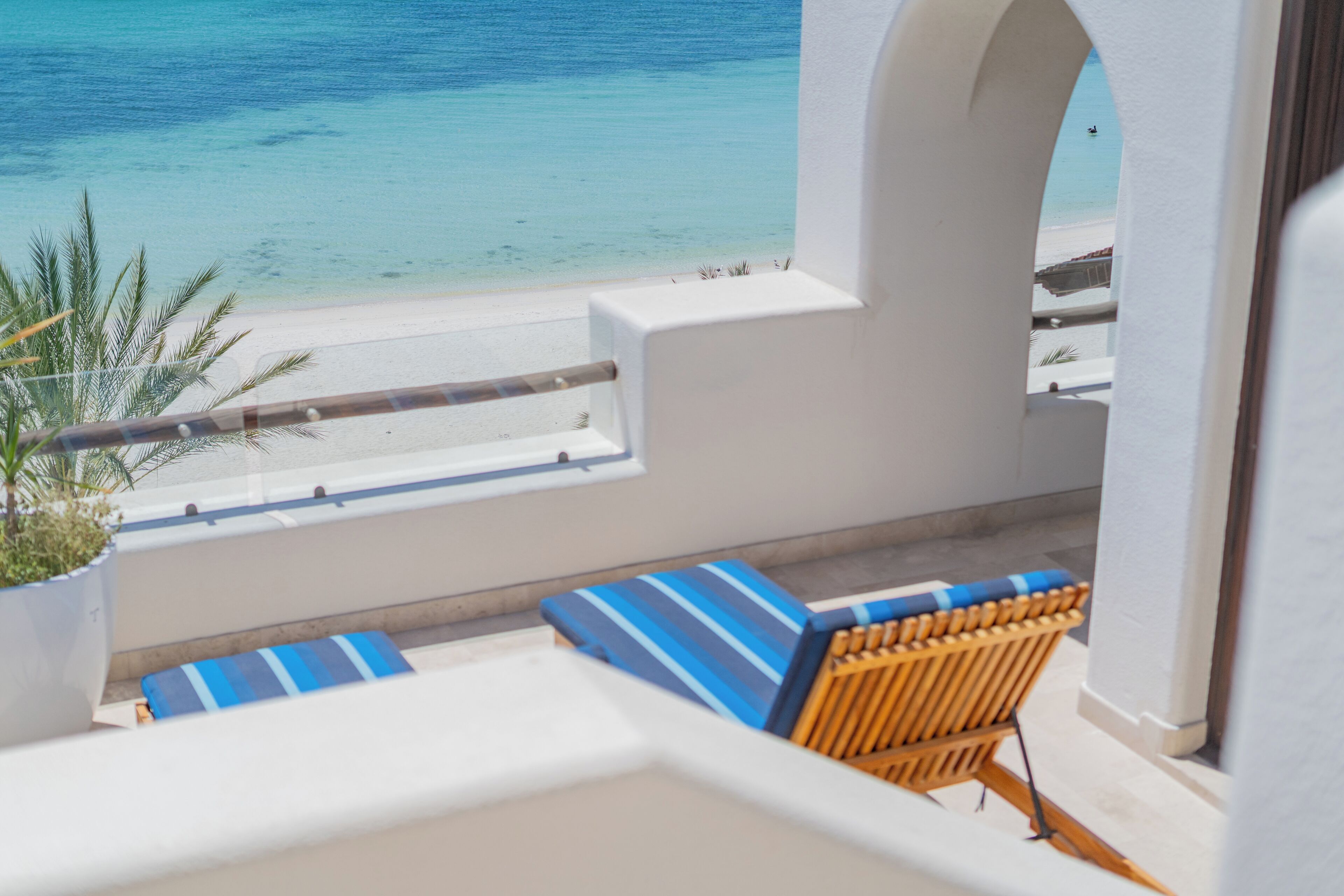 Un balcón con vistas al mar, una pared blanca y una silla de madera con cojines a rayas.