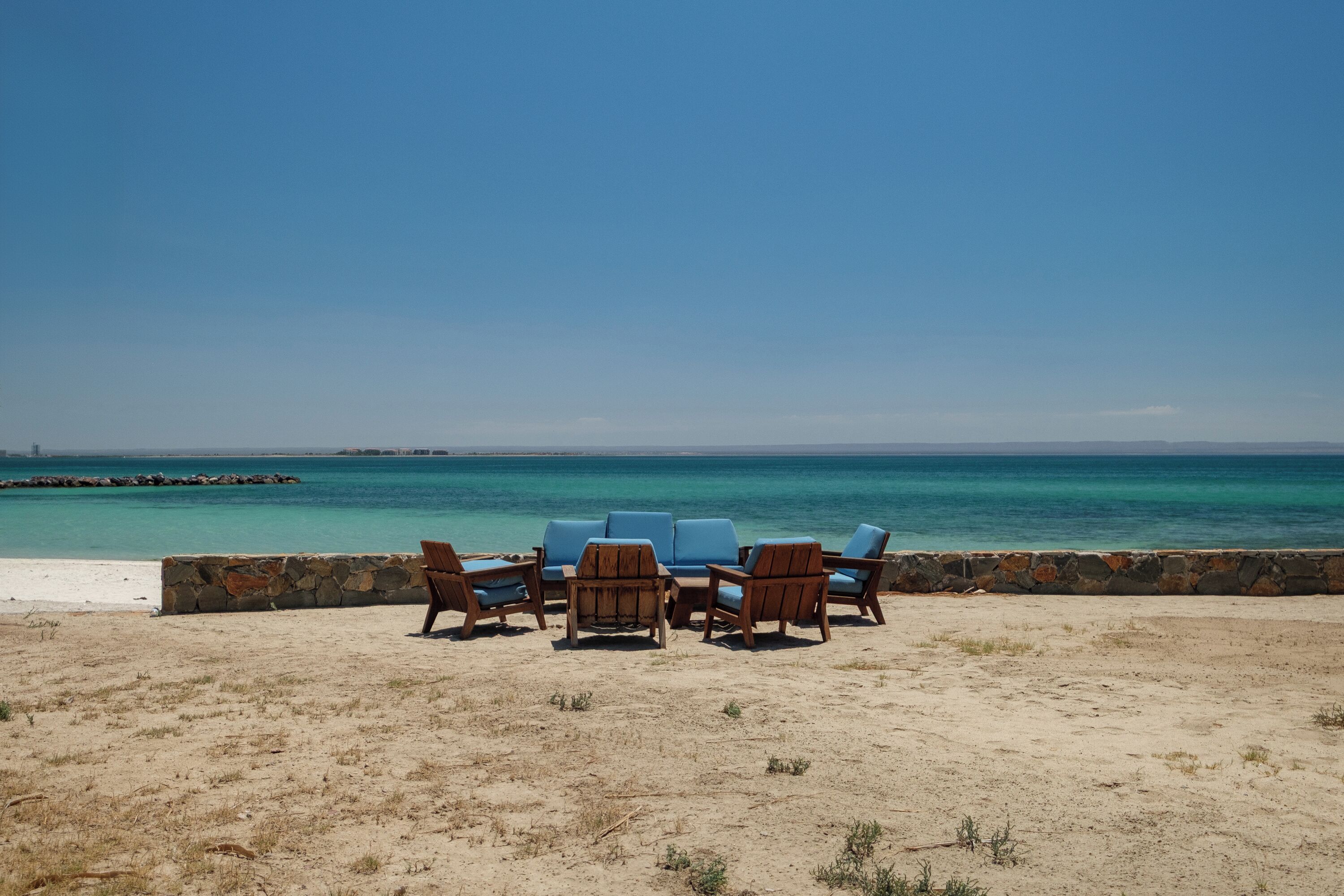 A beach with a stone wall and wooden chairs facing the ocean.
