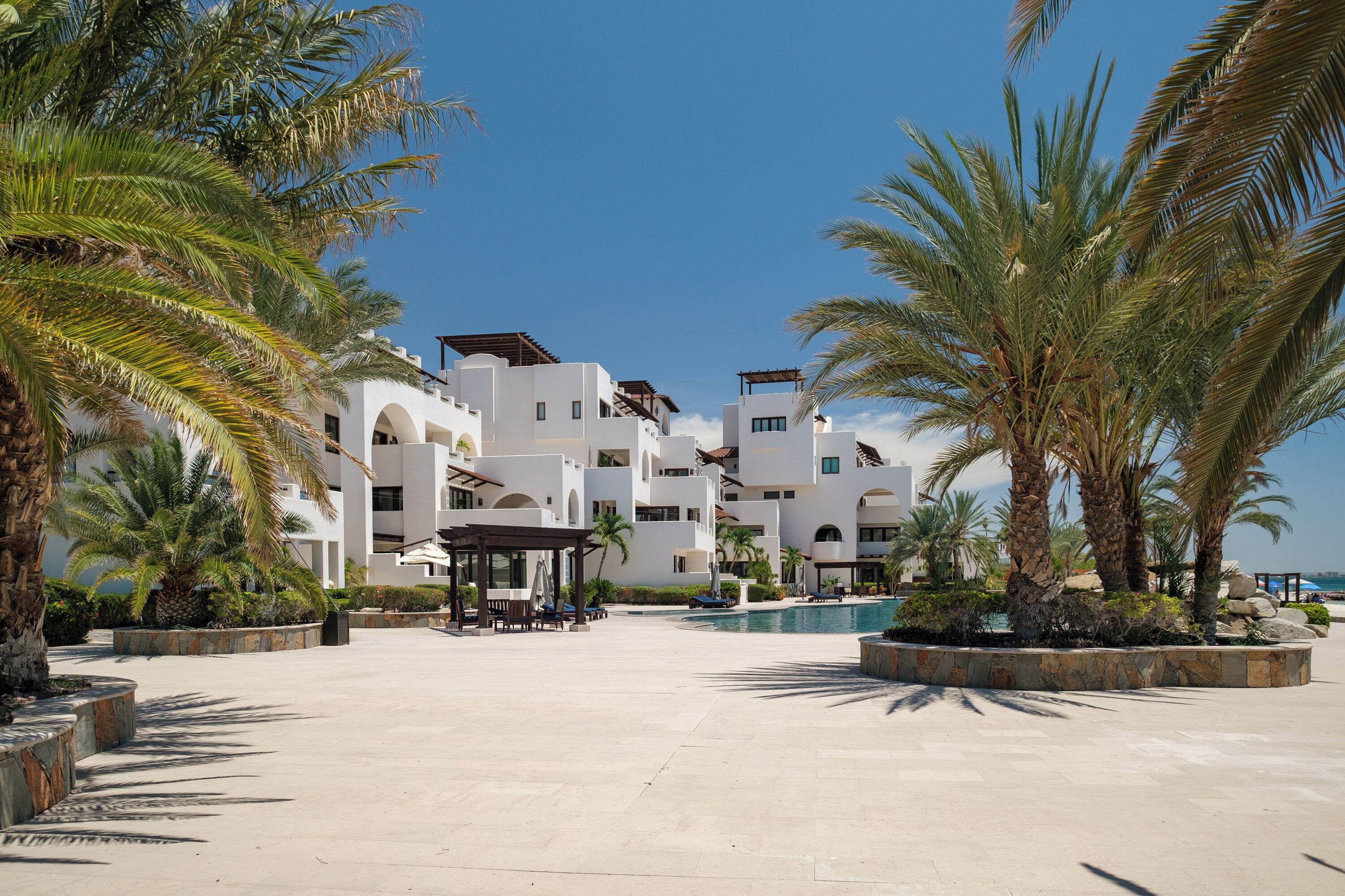 A resort with white buildings, a pool, and palm trees.