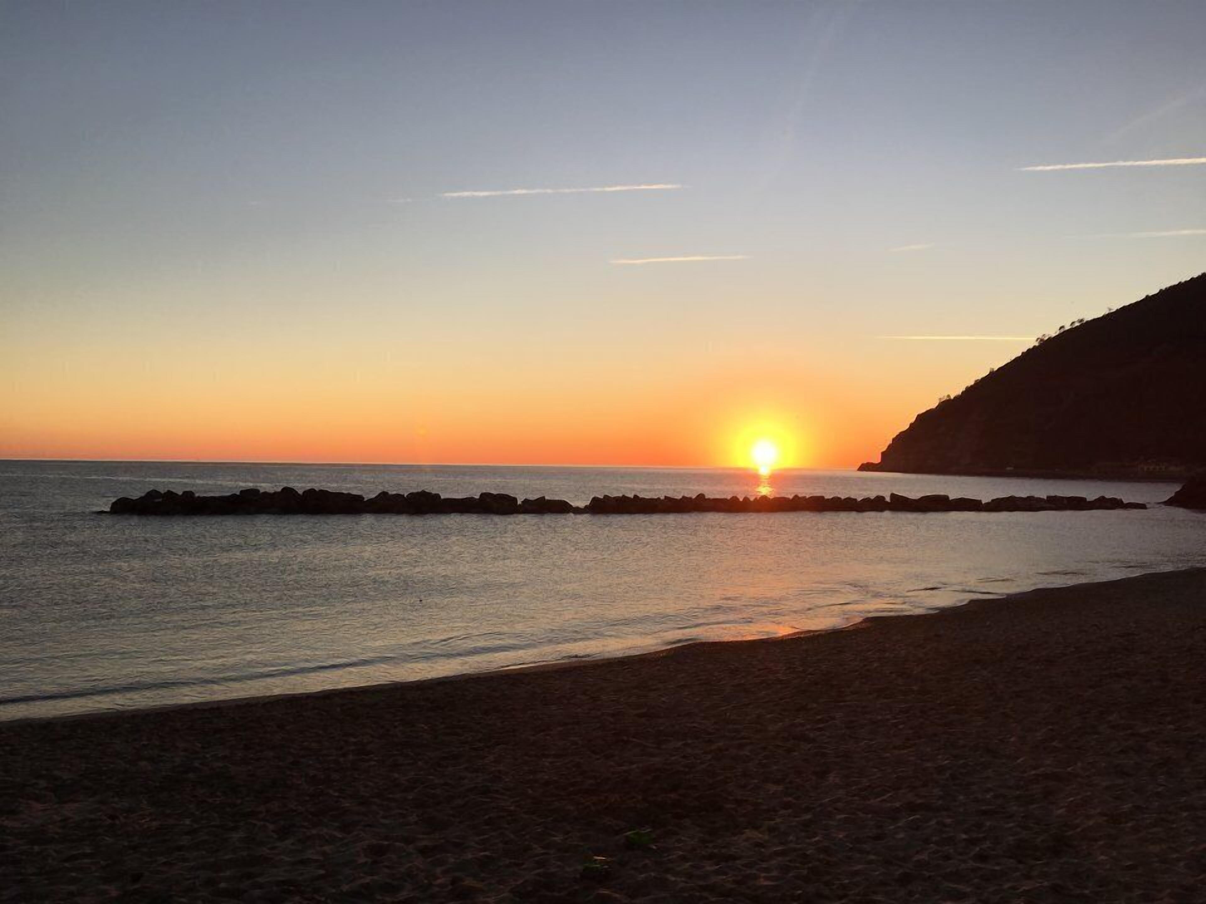A sunset over a beach with a rocky breakwater and a cliff in the background.