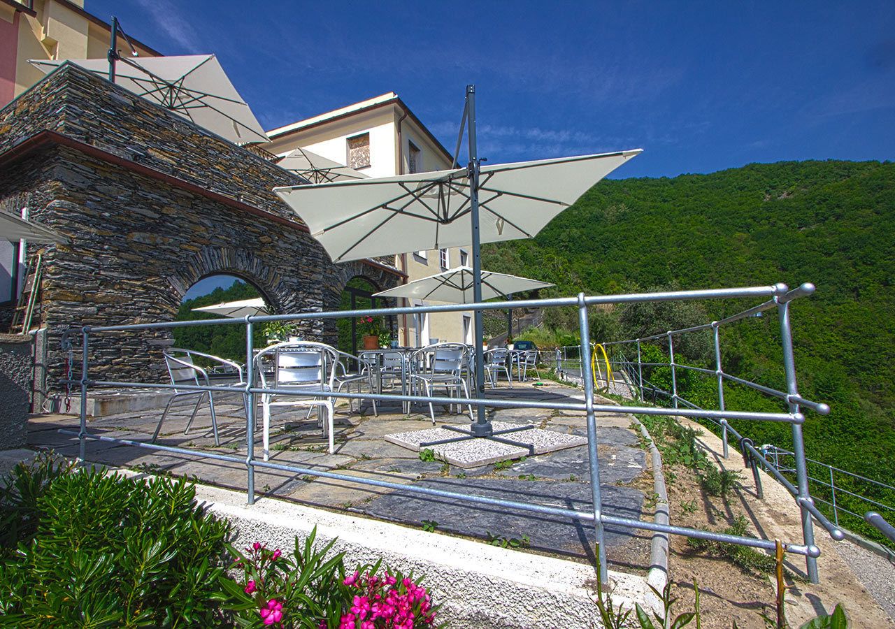 A stone archway leading to a terrace with outdoor seating and a view of a hillside.